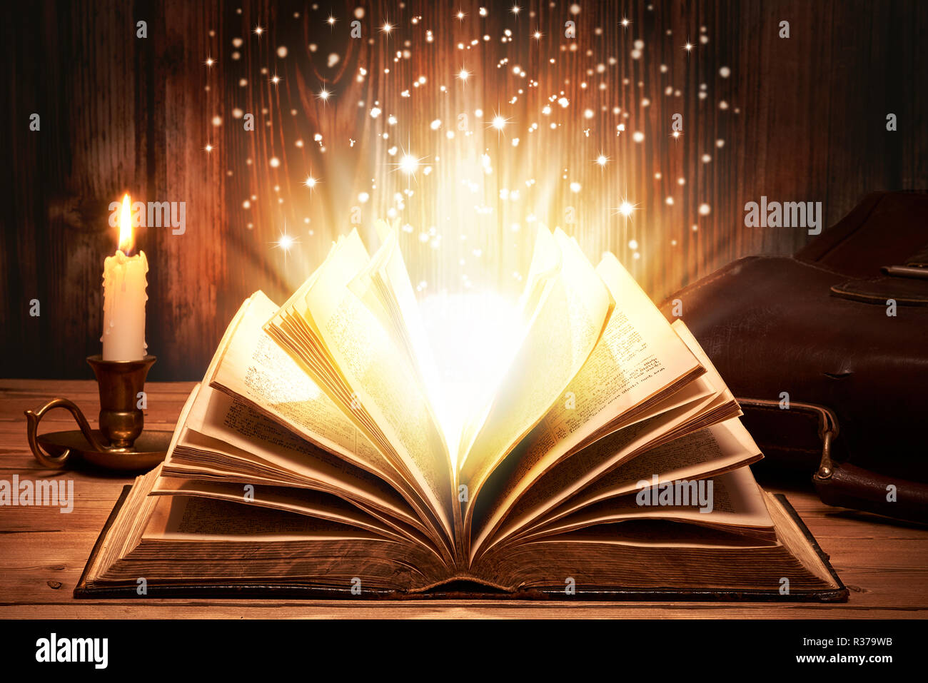 Old book with magic lights on wooden table by candlelight Stock Photo