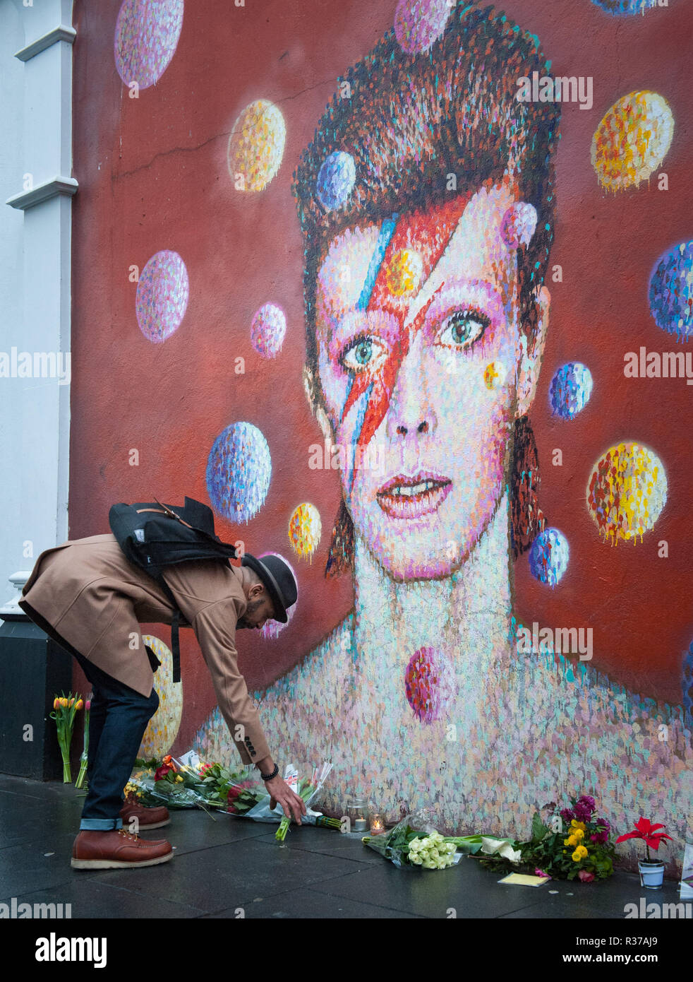 Tunstall Road, London, UK. 11th January, 2016. London, UK. Mourners lay flowers at  the foot of the David Bowie mural in Brixton.  Pictured: A man lay Stock Photo
