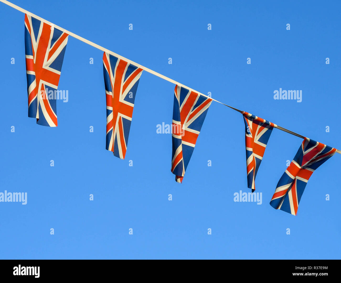 Row of small Union Jack flags fluttering in the wind against a deep blue sky. Stock Photo
