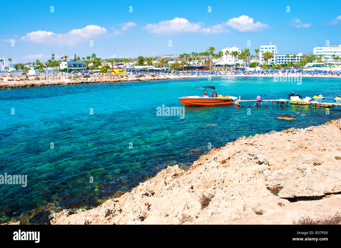 Image of one red speedboat in the bay of Vathia Gonia beach near Agia Napa, Cyprus. Rocky coast and sea with turquoise blue water in a bay, houses on  Stock Photo