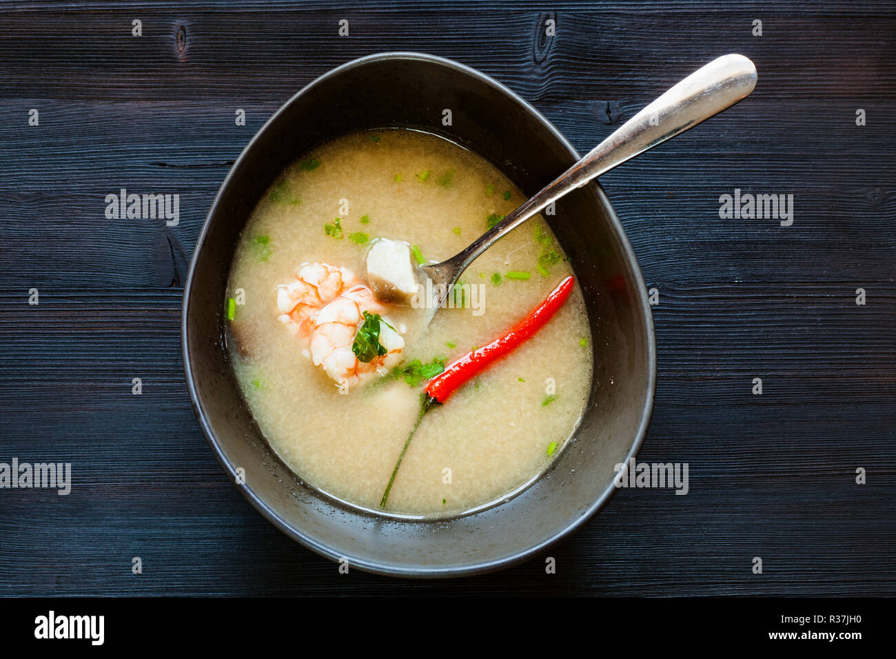 Thai cuisine dish - top view of bowl with Tom Kha Thale (Tom kha kai, Tom Kha Gai, Thai Coconut Soup) sour and spicy soup with shrimps and mushrooms o Stock Photo