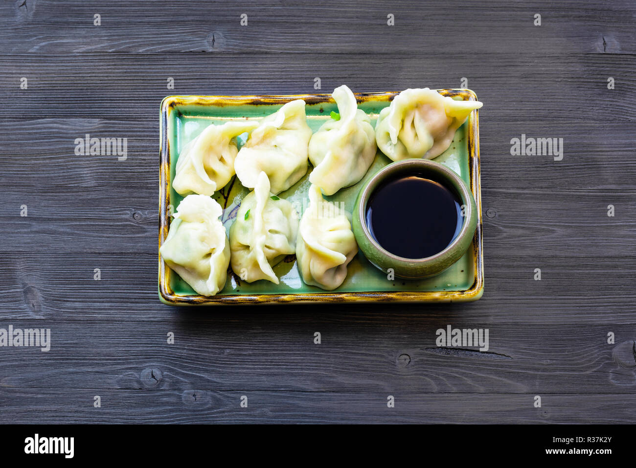 Chinese cuisine dish - top view of served portion of Dumplings with three fillings (shrimp, egg and greens) on green plate on dark wooden board Stock Photo