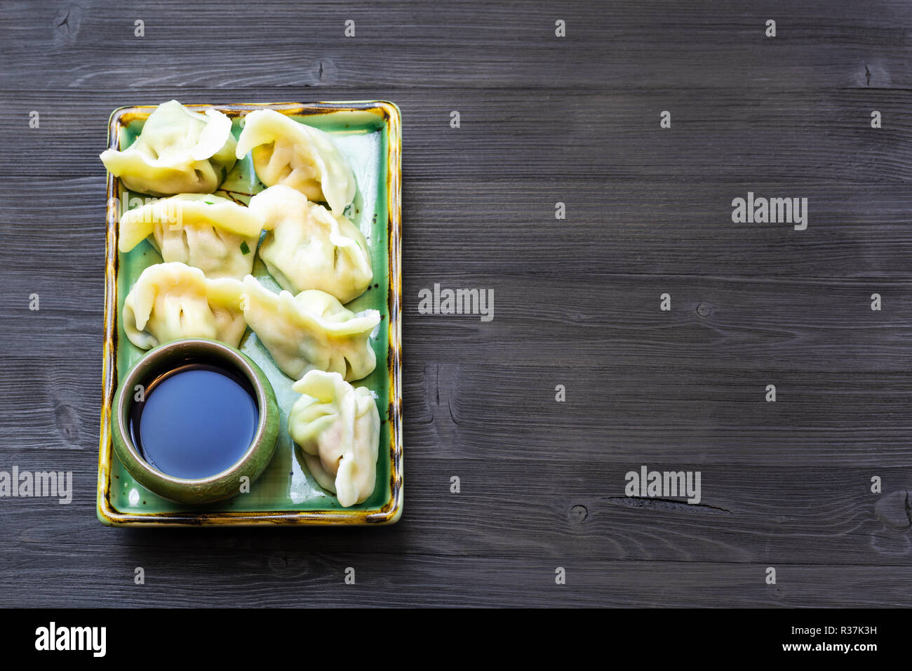 Chinese cuisine dish - served portion of Dumplings with three fillings (shrimp, egg, greens) on plate on dark wooden board with copyspace Stock Photo