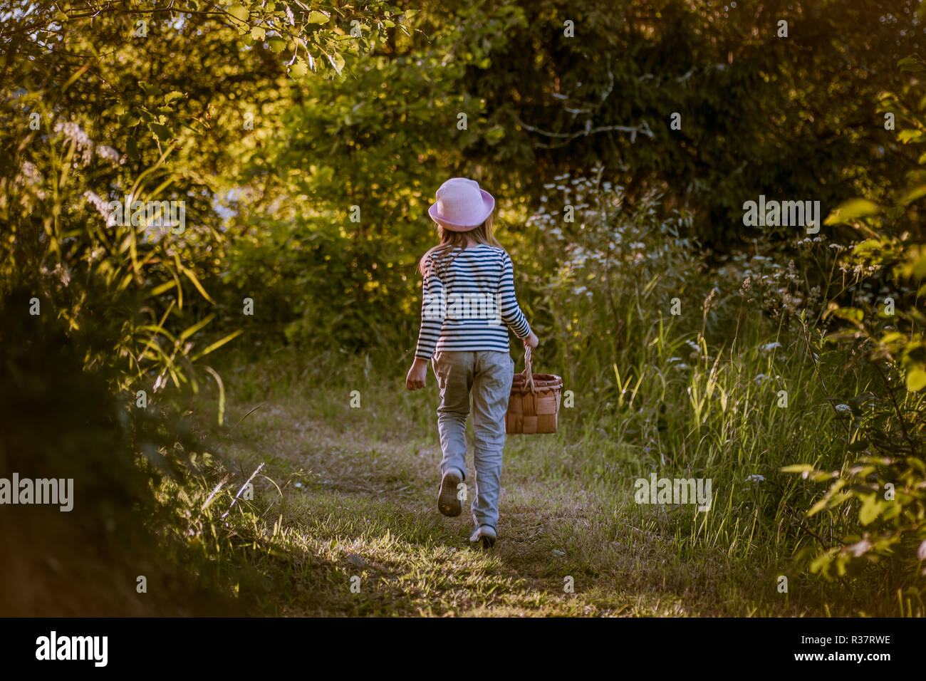 Young girl walking on a path through green woods carrying a basket ...