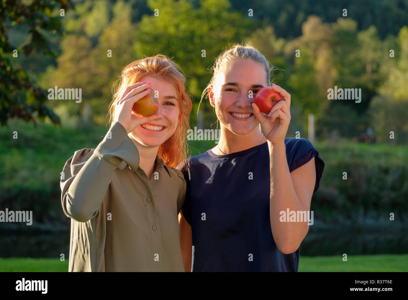 Two girls, young women, laughing eating apples, in the garden, Upper Bavaria, Bavaria, Germany Stock Photo