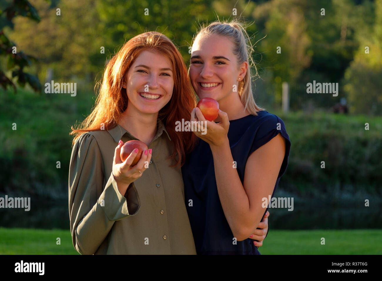 Two girls, young women, laughing eating apples, in the garden, Upper Bavaria, Bavaria, Germany Stock Photo