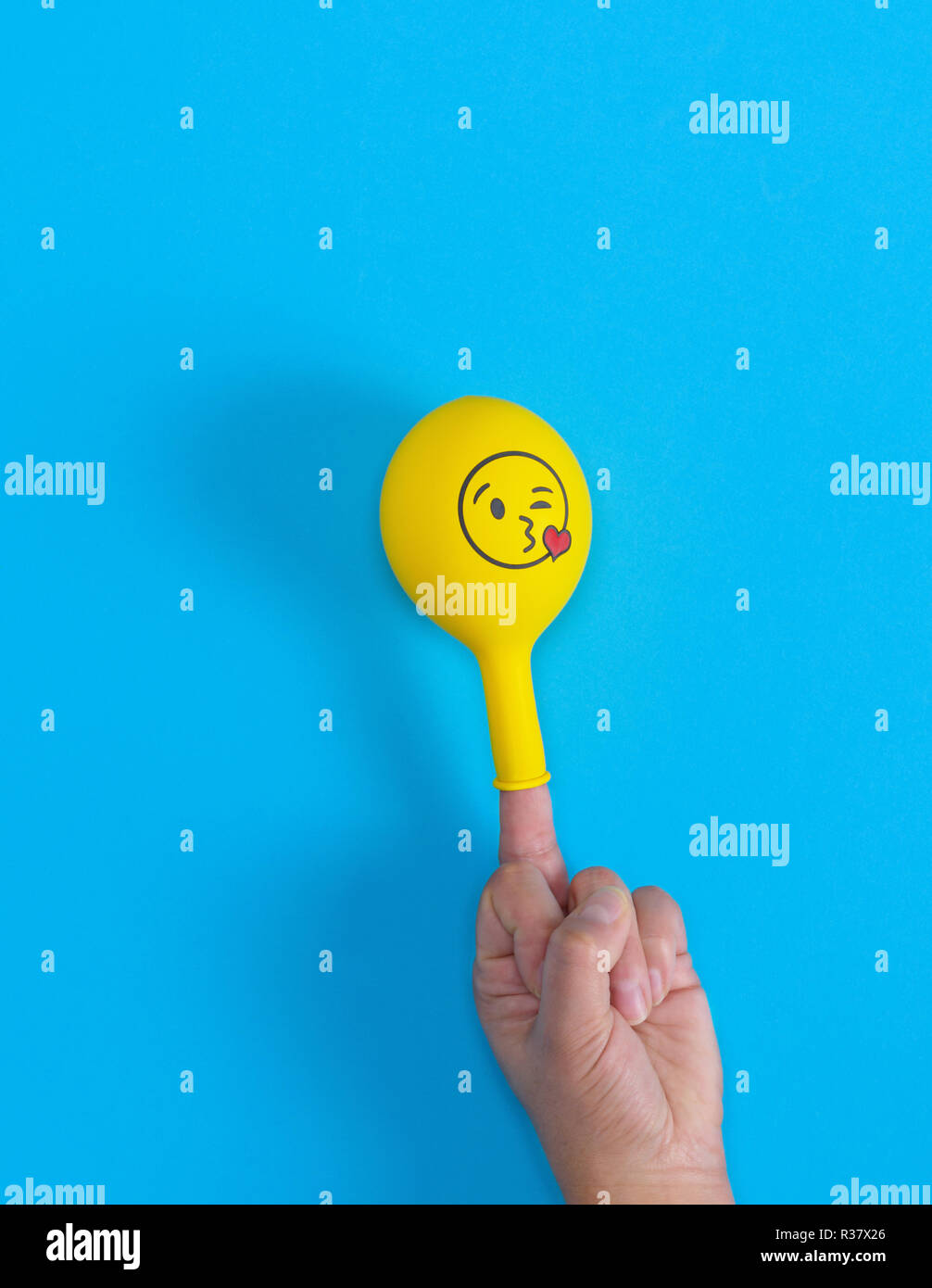 yellow inflated ball dressed on the middle finger of a human hand, blue background Stock Photo