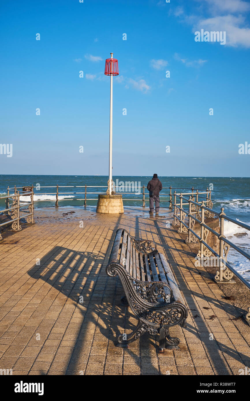 A rear view of a man on his own standing looking over the English Channel on the end of a jetty in Swanage, Dorset, England, UK Stock Photo