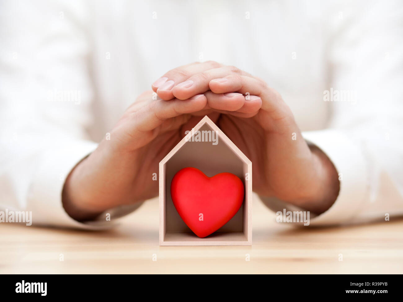 Wooden house with red heart protected by hands Stock Photo