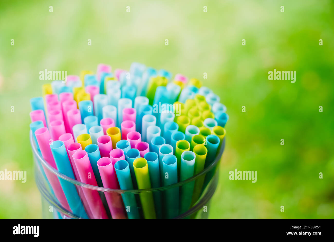 Bright colorful cocktail beverage straws and tubes put together in the big glass on green grass summer background. Preparing to the party Stock Photo