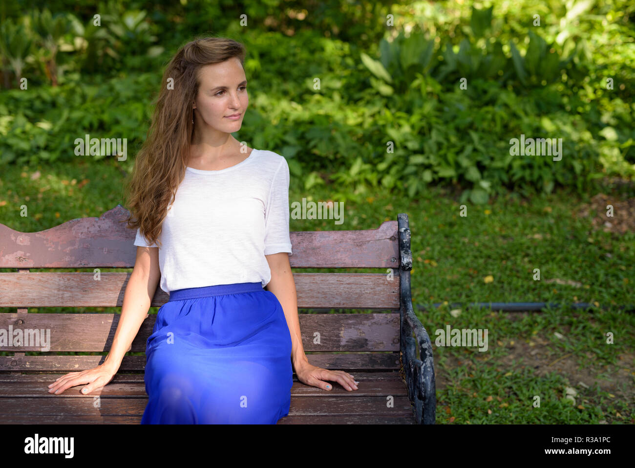 Beautiful woman with long hair thinking while sitting on wooden  Stock Photo