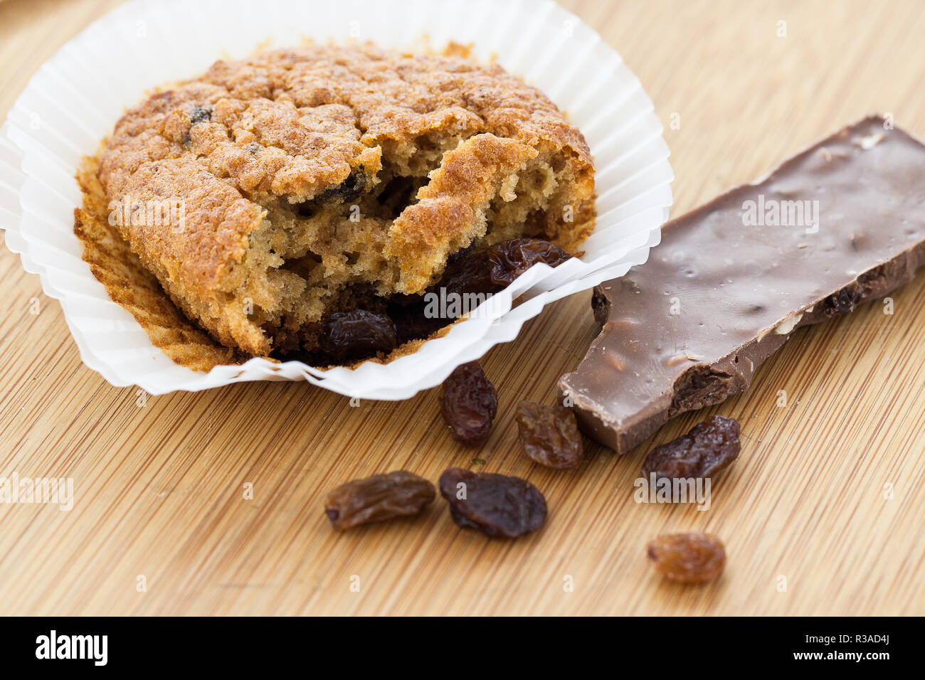 a bitten chocolate biscuit in a white paper form lies on a wooden background,together with raisins and a piece of chocolate. Stock Photo