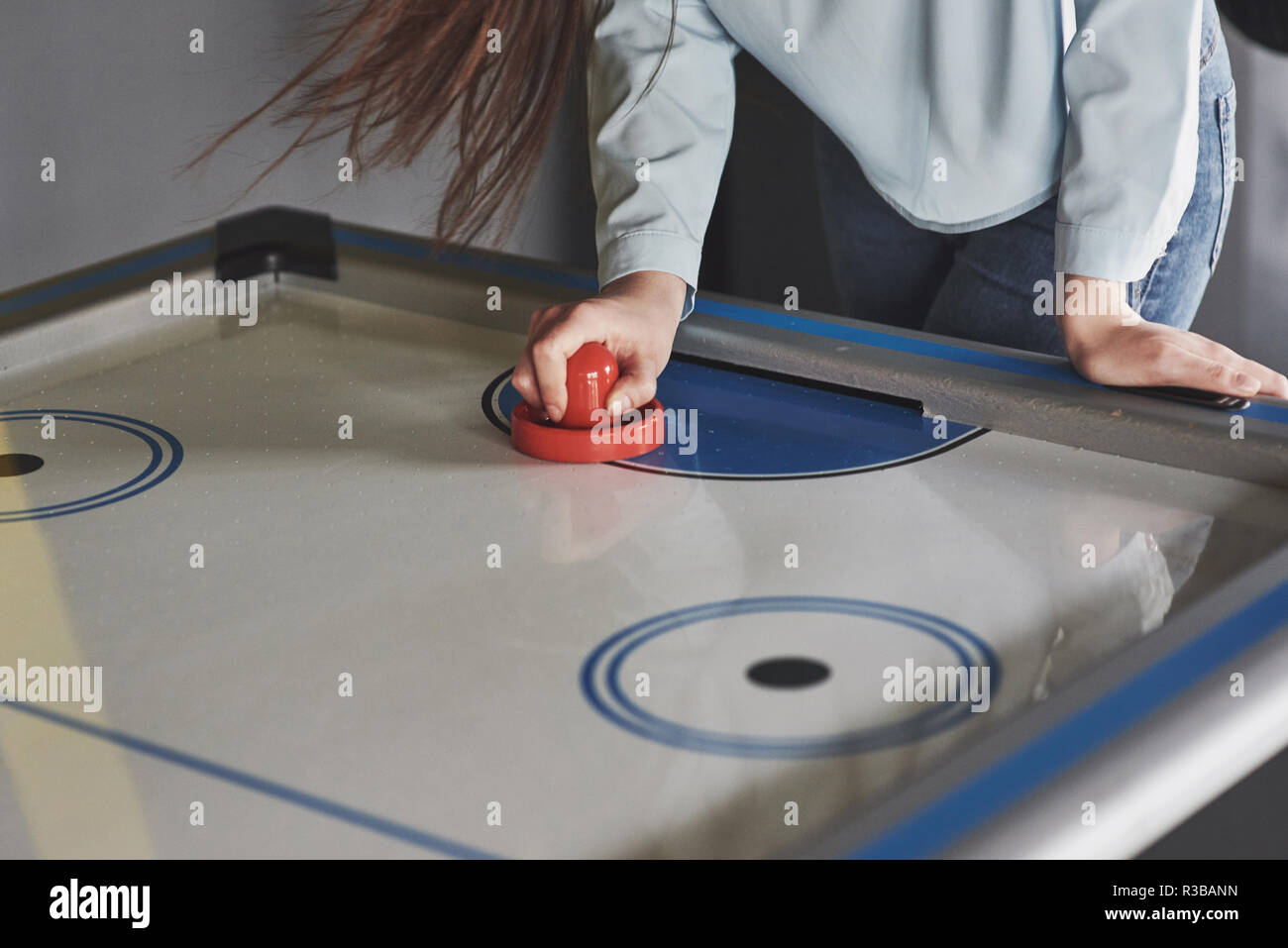 Hands of young people holding striker on air hockey table in game room