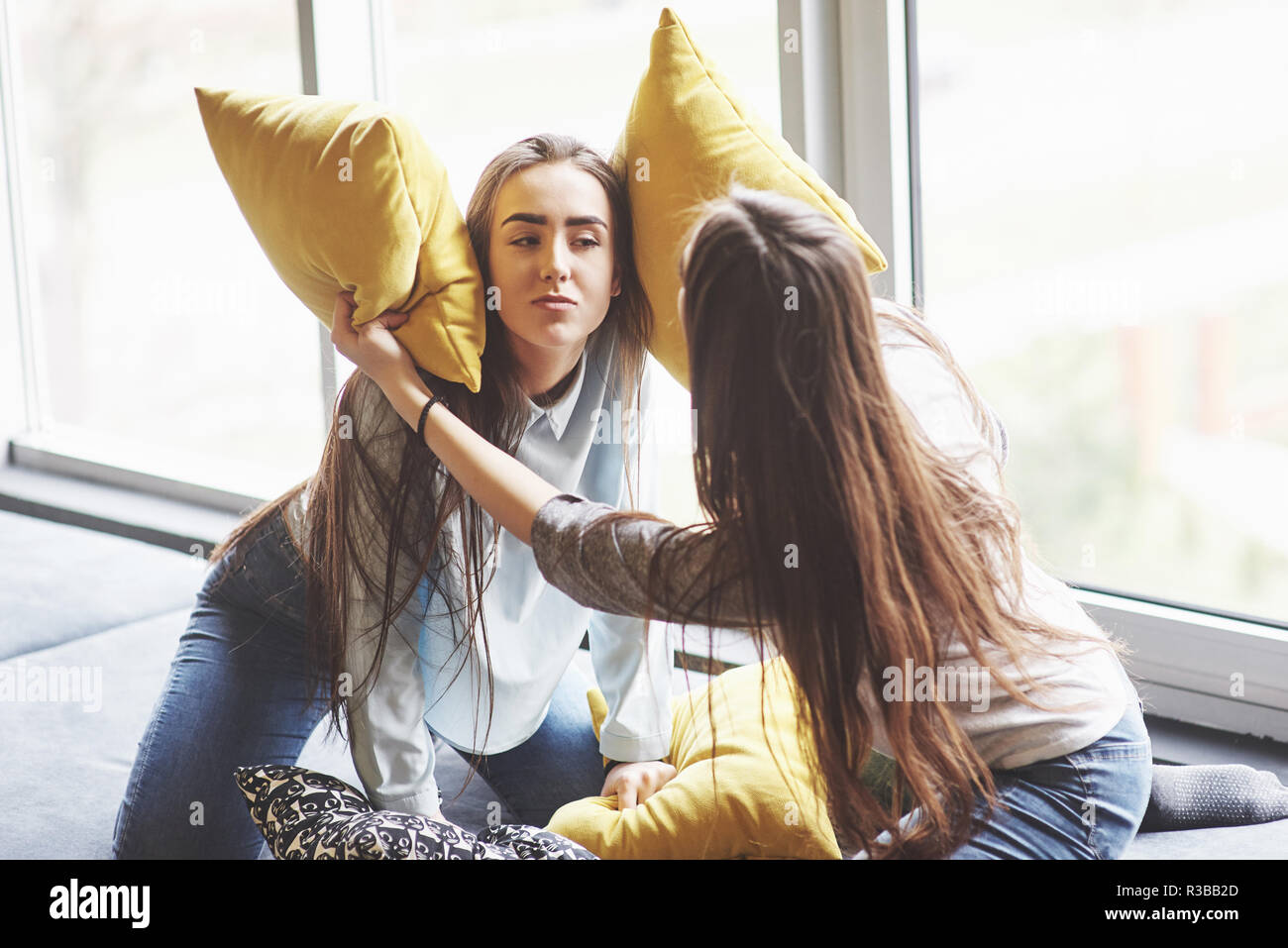 Two beautiful young twins sisters spending time together with pillows. Siblings having fun at home concept Stock Photo