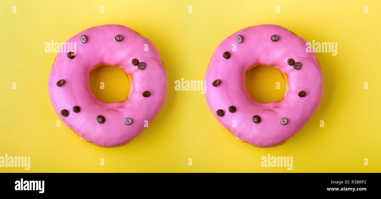 two donuts with pink icing on a yellow background Stock Photo
