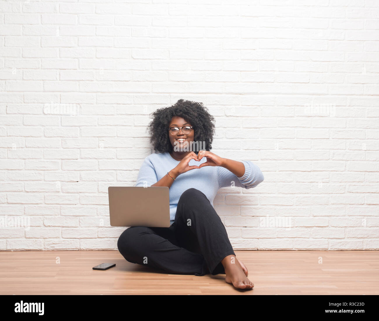 Young african american woman sitting on the floor using laptop at home ...