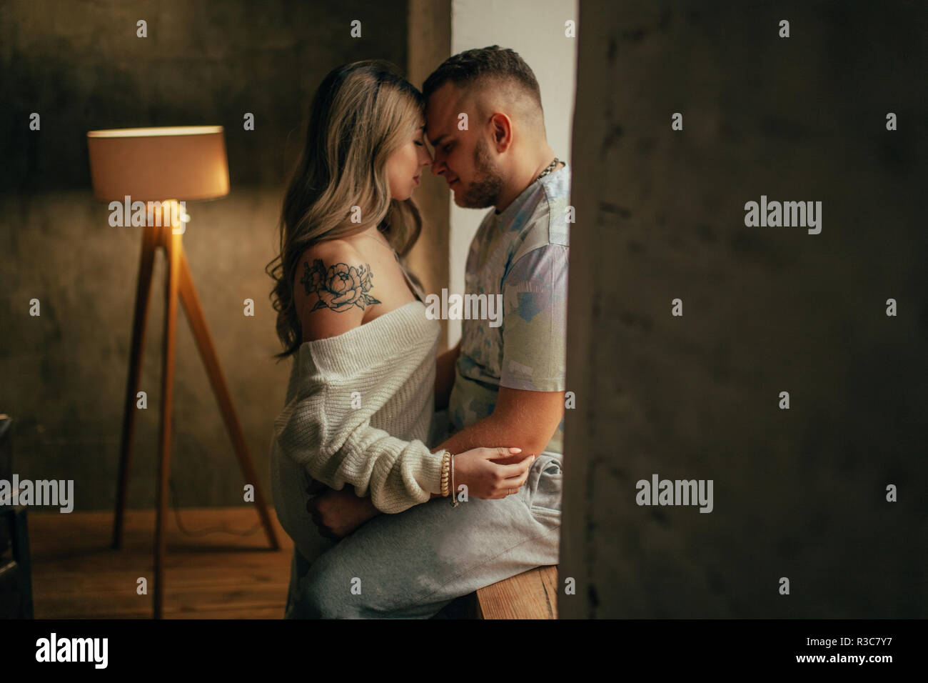 A young couple in love is hugging in front of the window face to face on background of torchere. Stock Photo