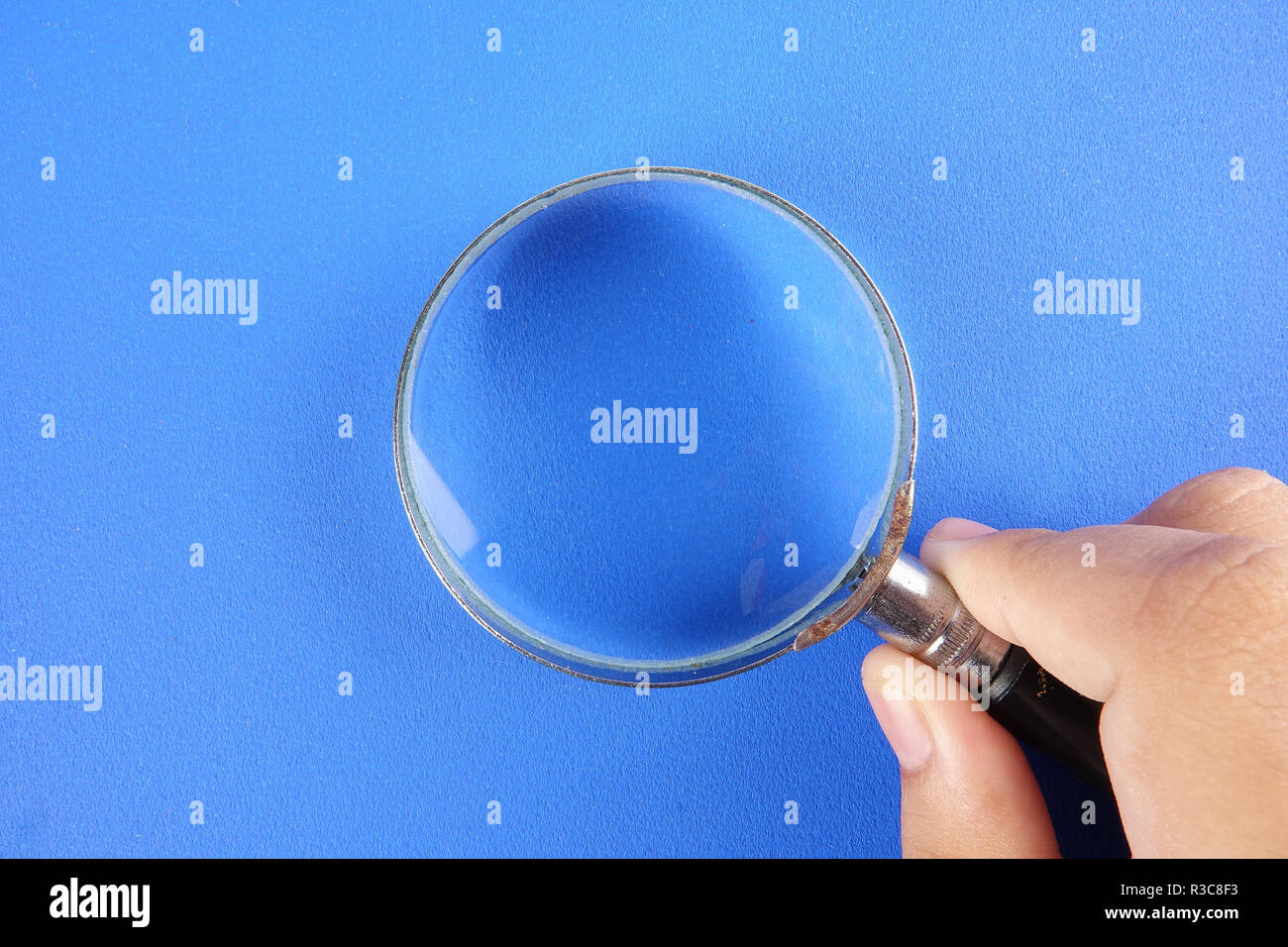 Hand holding magnify glass over a blue background Stock Photo