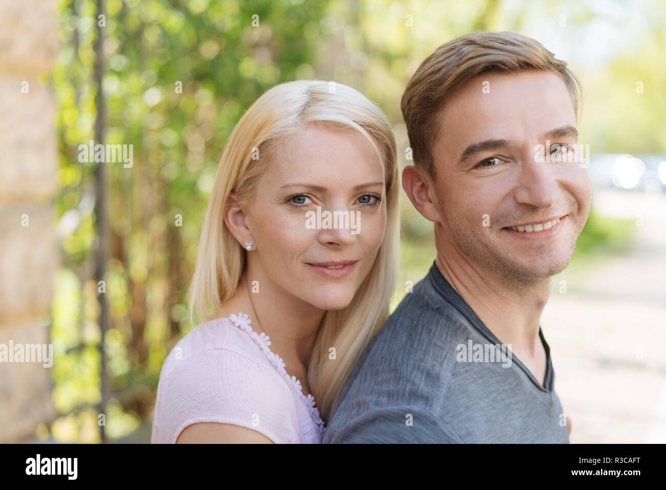 Attractive young couple standing close together turning to smile at the camera outdoors in a rural road Stock Photo