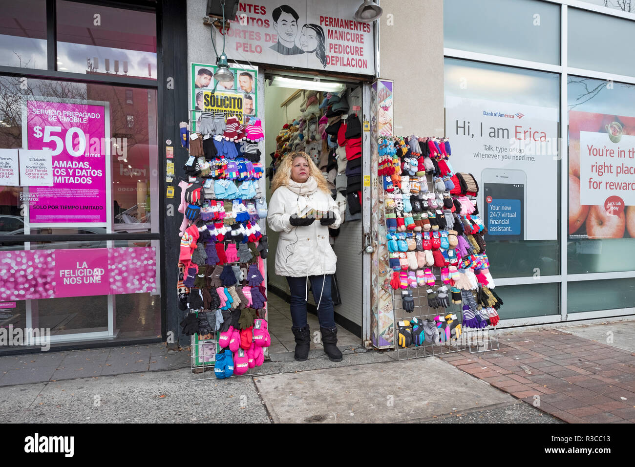 A blonde Latin American woman hands out leaflets outside a hair salon & tchotchke shop on Junction Boulevard in North Corona, Queens, New York City. Stock Photo