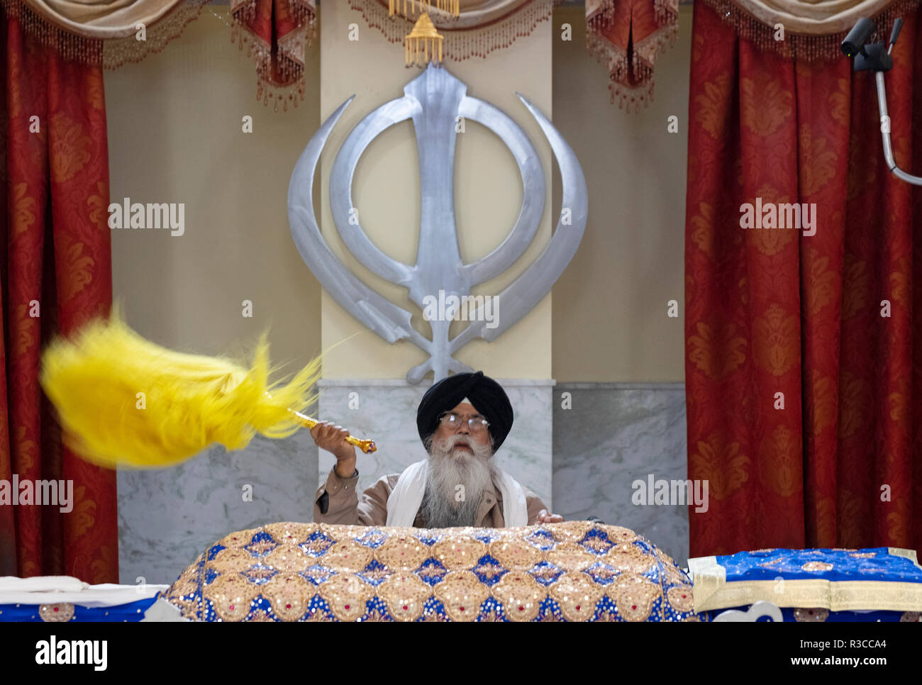 A Sikh priest waving a yellow flag - chaur sahib - during afternoon services at a temple in Richmond Hill, Queens, New York. Stock Photo