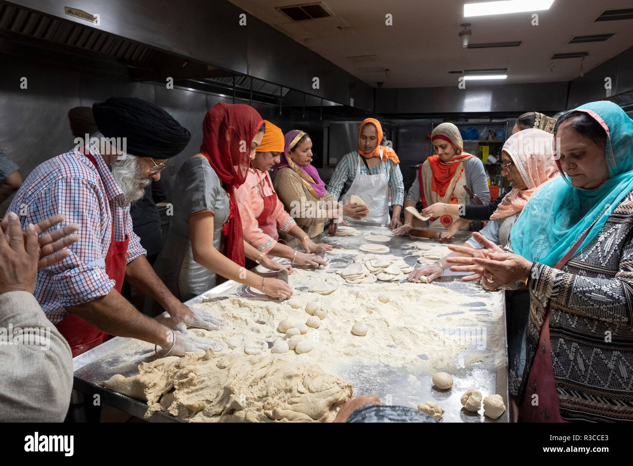 A group of Sikh men & women volunteers, make roti for a langar, a free ...