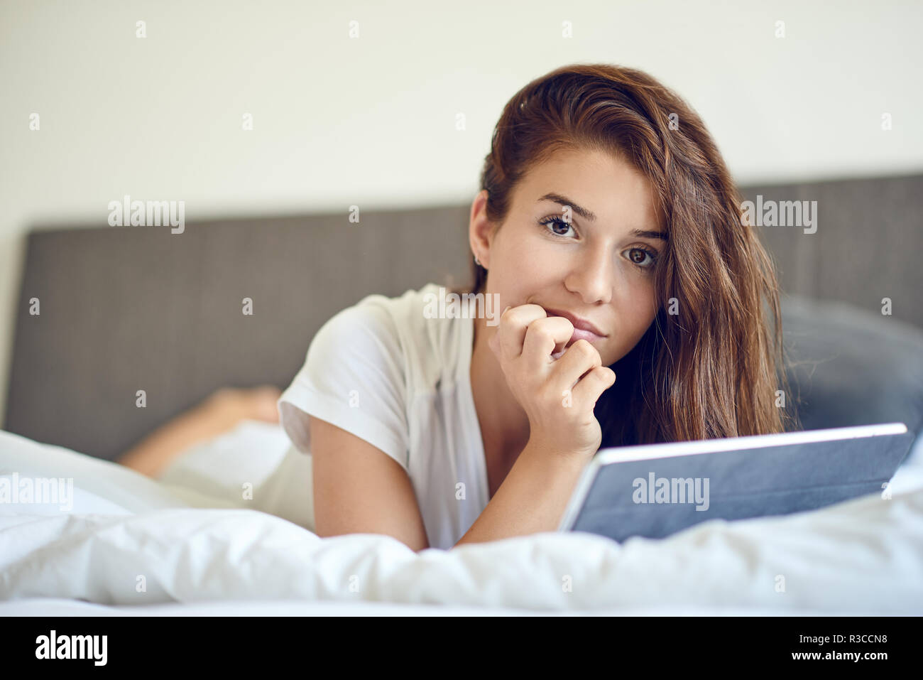 Beautiful young woman in white tshirt laying on stomach in bed, with