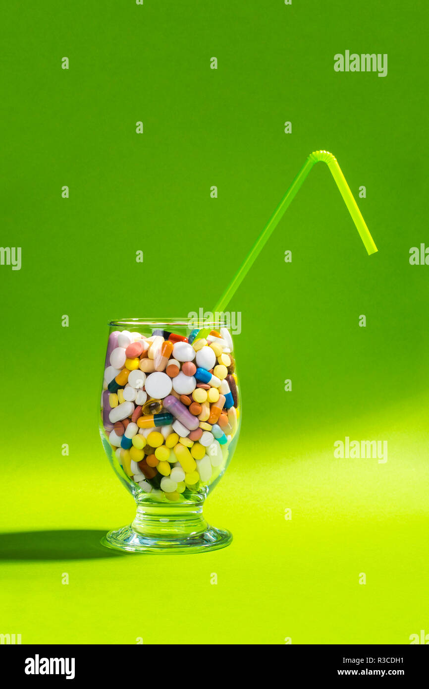 Glass full of colorful pills with green straw. Creative composition. Stock Photo