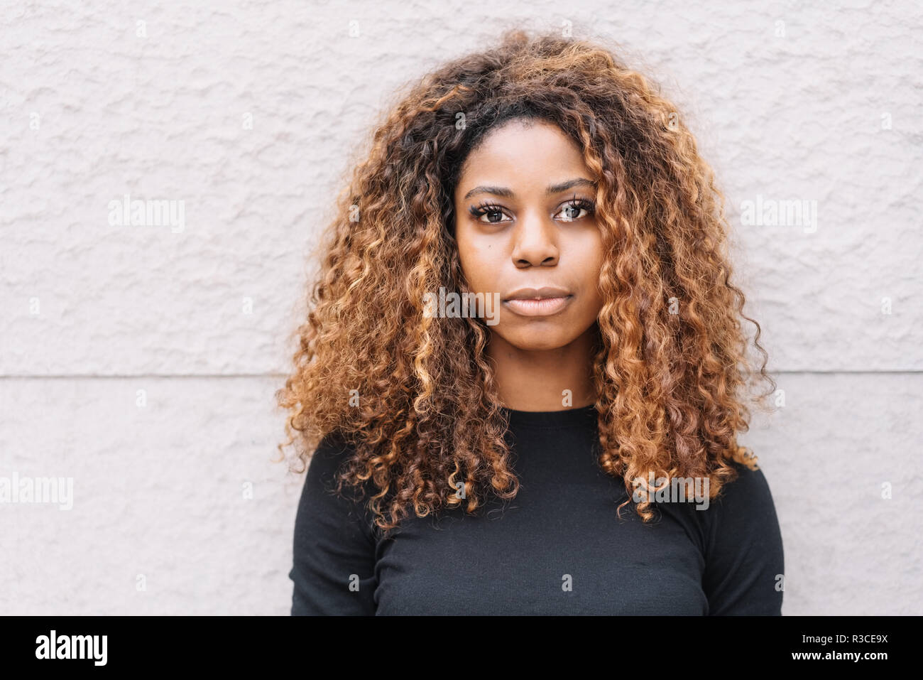 Serious young African woman with gorgeous long curly hair standing against  a rough plaster wall staring at the camera Stock Photo - Alamy