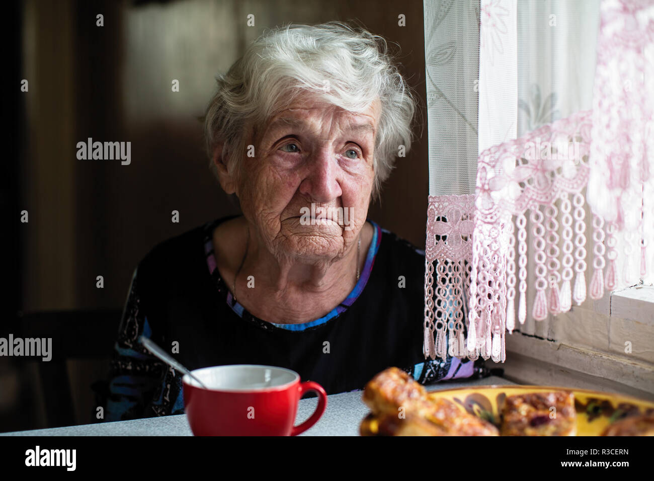 Retired elderly woman in the kitchen of his house sitting at the table ...