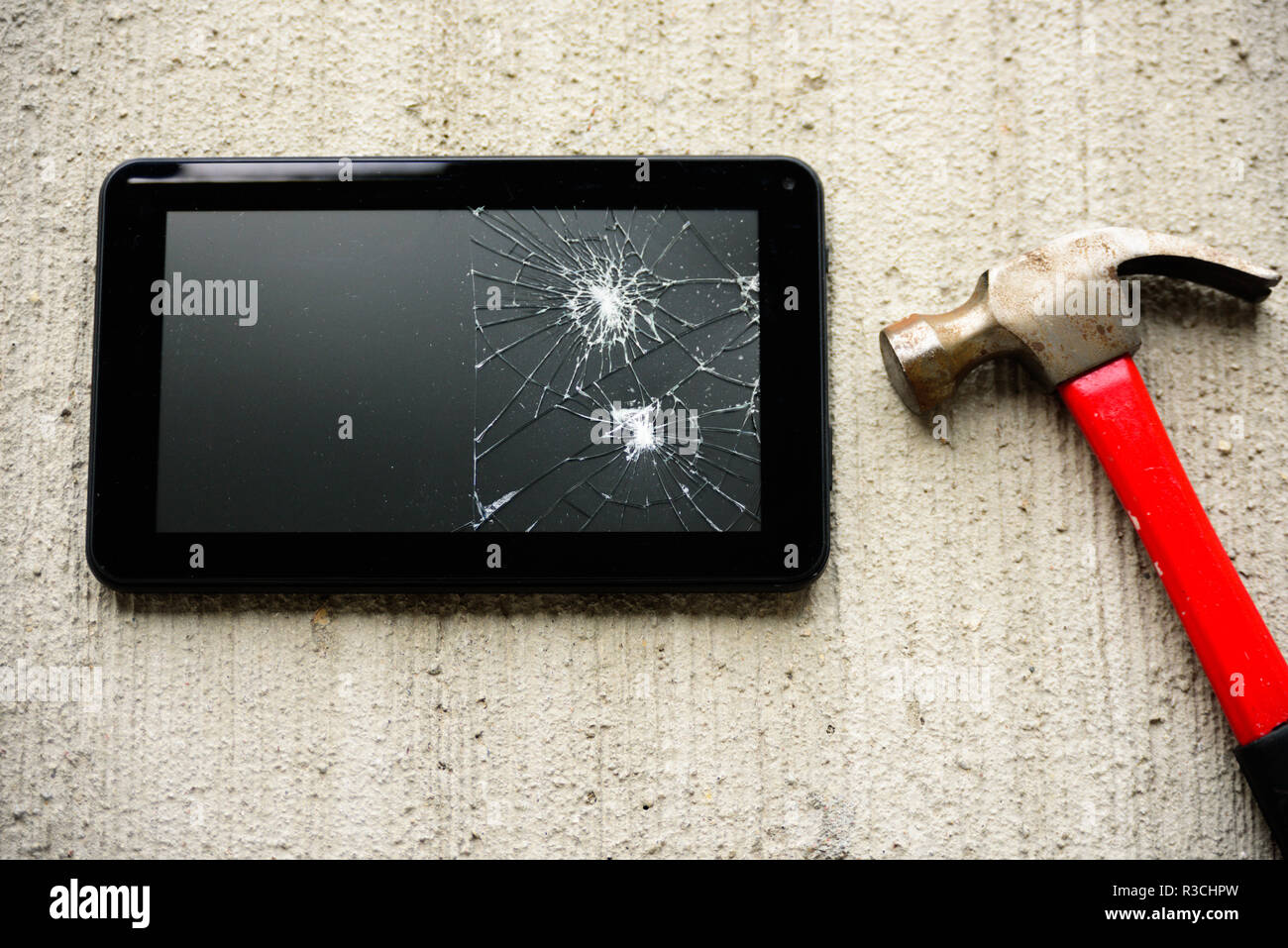 Broken tablet screen with red rusty hammer near it on concrete background Stock Photo