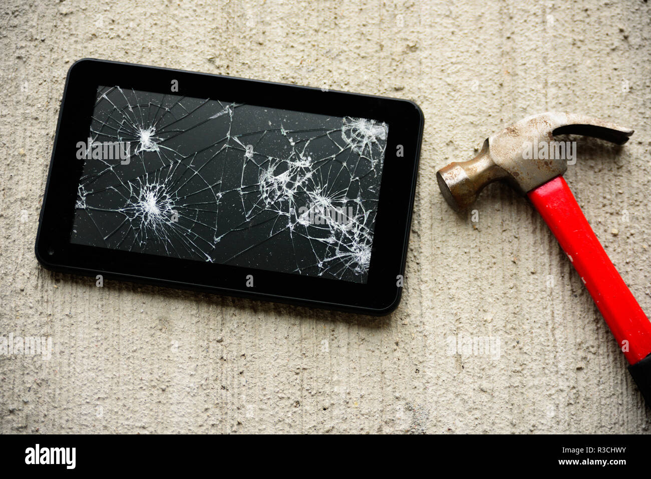 Broken tablet screen with red rusty hammer near it on concrete background Stock Photo