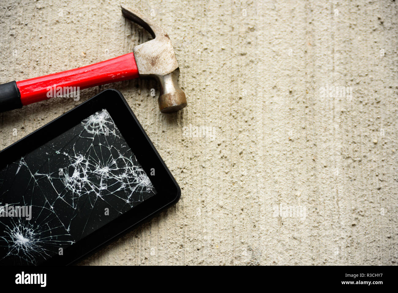 Broken tablet screen with red rusty hammer near it on concrete background Stock Photo