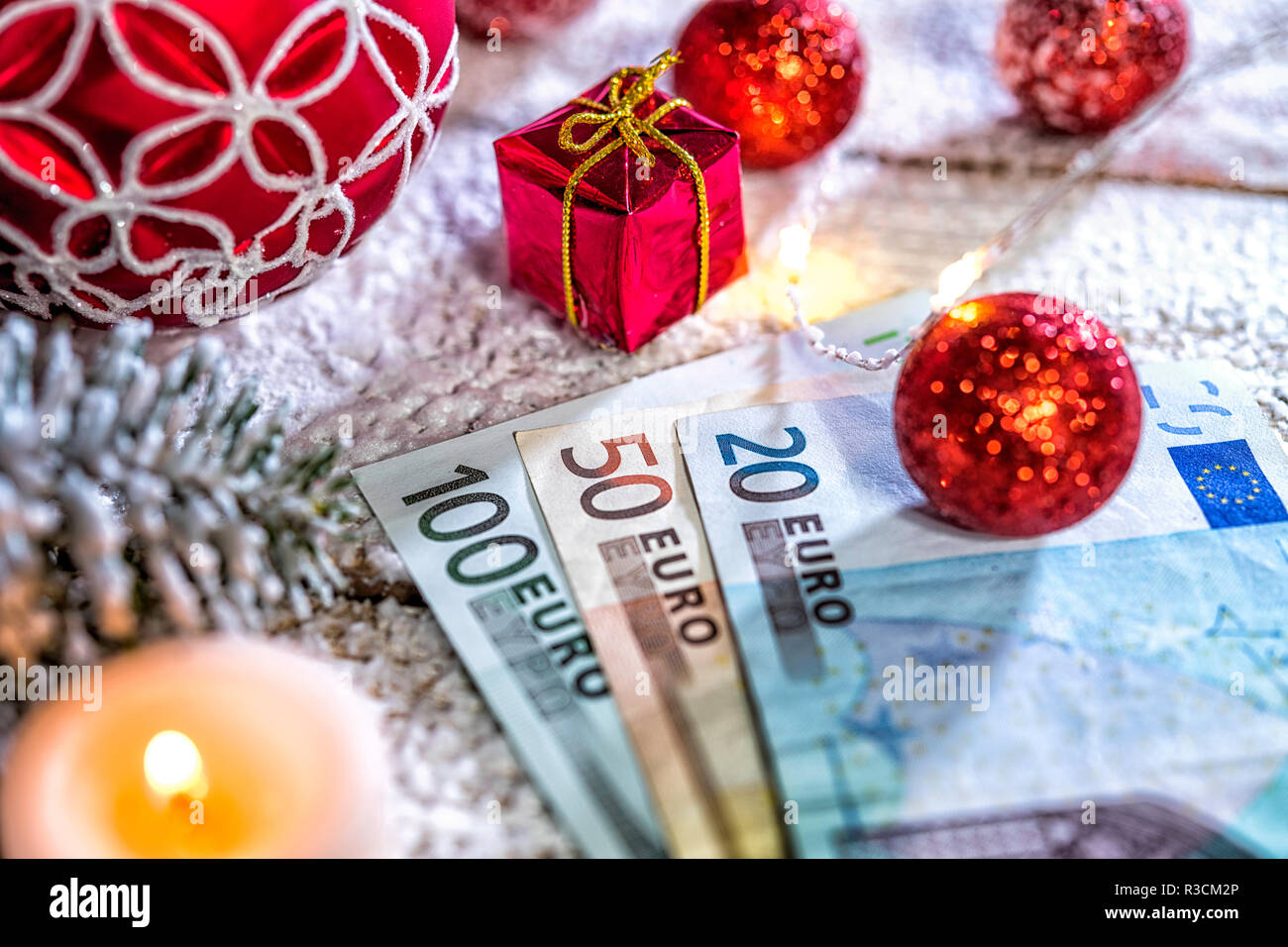 Christmas ball on old wooden table with candle and Euro banknotes Stock Photo