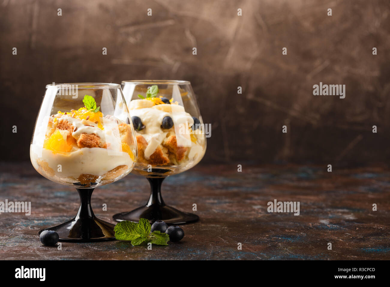 Two glasses with Healthy homemade layered dessert trifle with orange, blueberry, biscuit, yogurt and granola. Place for text Stock Photo