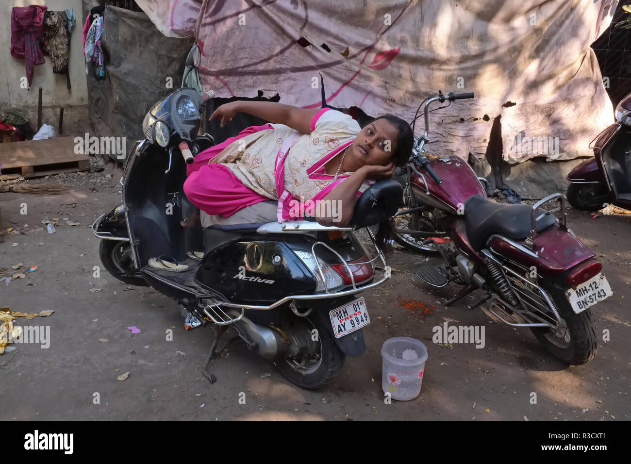 Its owner away, a slum dweller in Mumbai, India, makes herself comfortable on a motorcycle, the 'Press' sign indicating the owner is a journalist Stock Photo