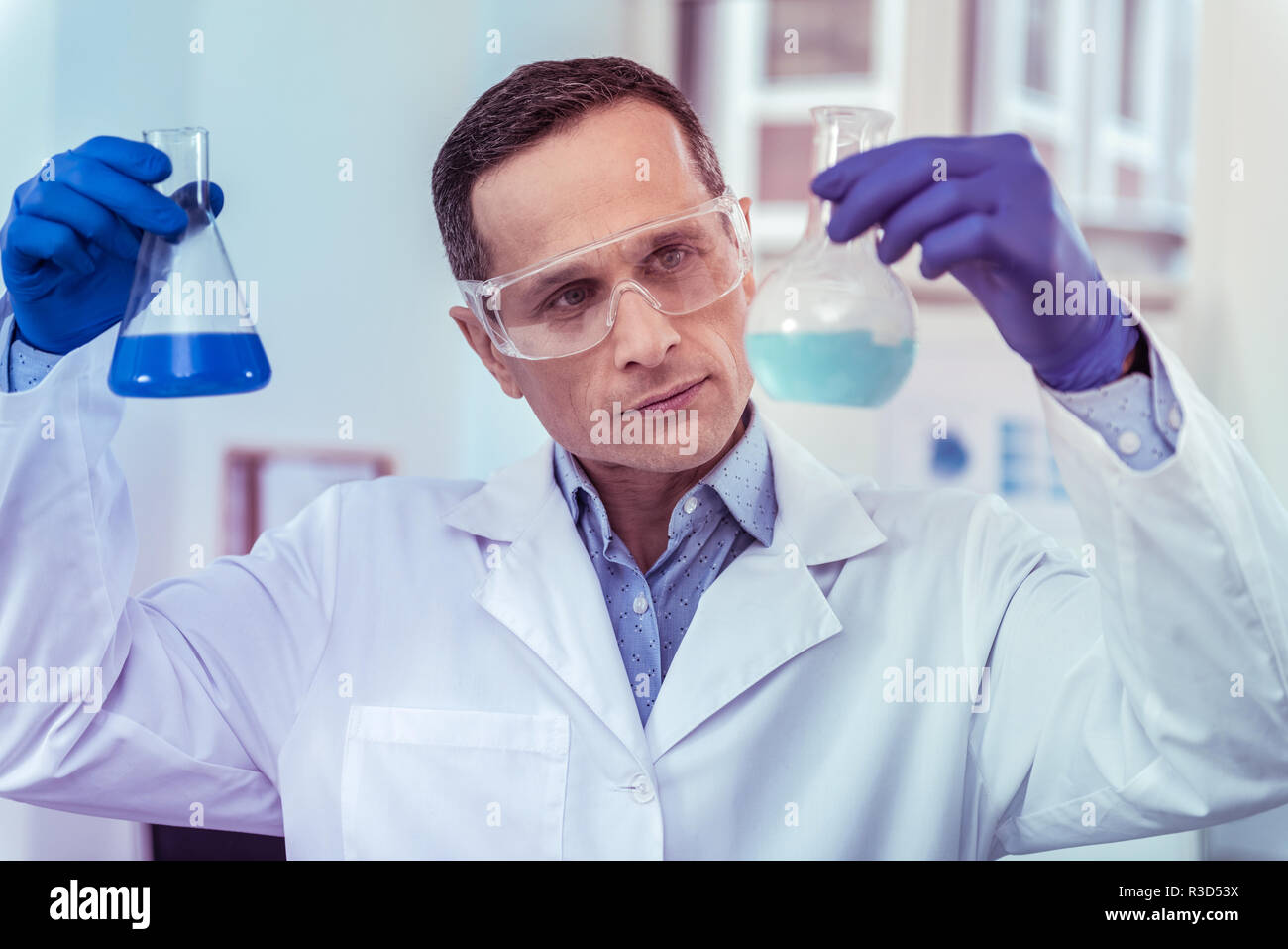 Great result. Kind man raising hands while looking at blue liquid Stock Photo