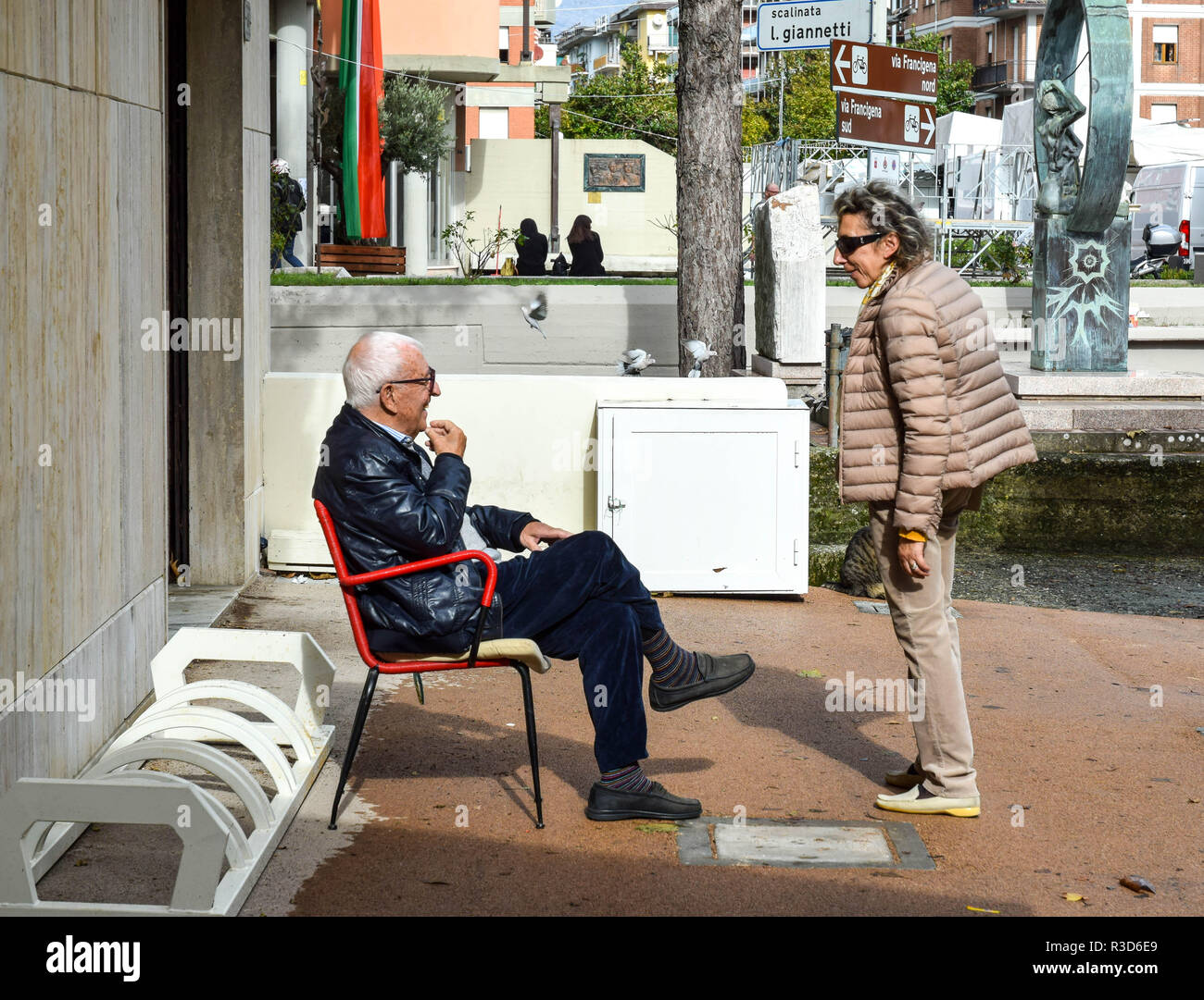 Conversation between old friends in Aulla, Tuscany. Man sits in retro-style red chair. Stock Photo