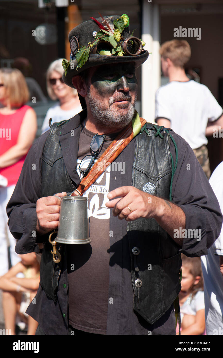 Box Hill Bedlam Morris dancer with blacked face and hops around his hat, standing while talking with beer tankard in his hand, Faversham Hop festival Stock Photo