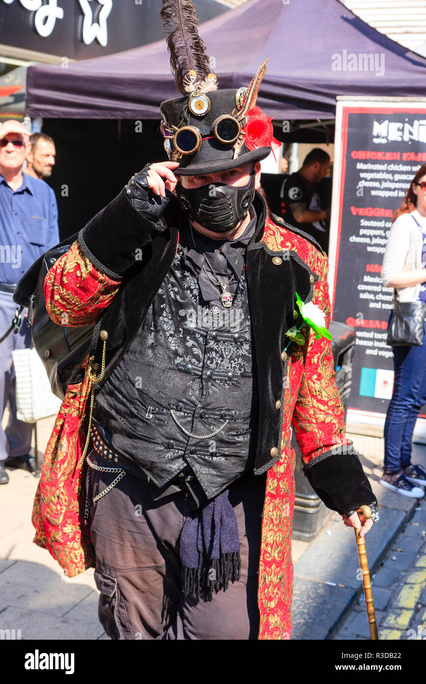 Steampunk man wears black with red jacket. Stands facing hand