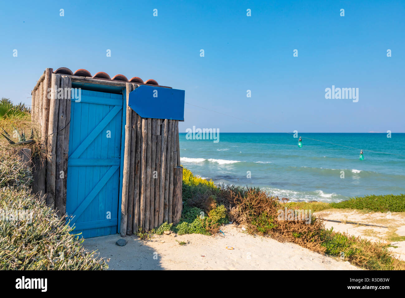 View of a small wooden cabin on the shore of the azure Mediterranean Sea, with a sign that can be used as a placeholder for your own personalised mess Stock Photo