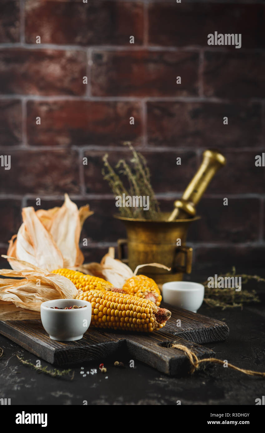 Yellow corn on cobs on grunge dark table, with Thyme, salt and pepper, closeup. Space for text. Stock Photo