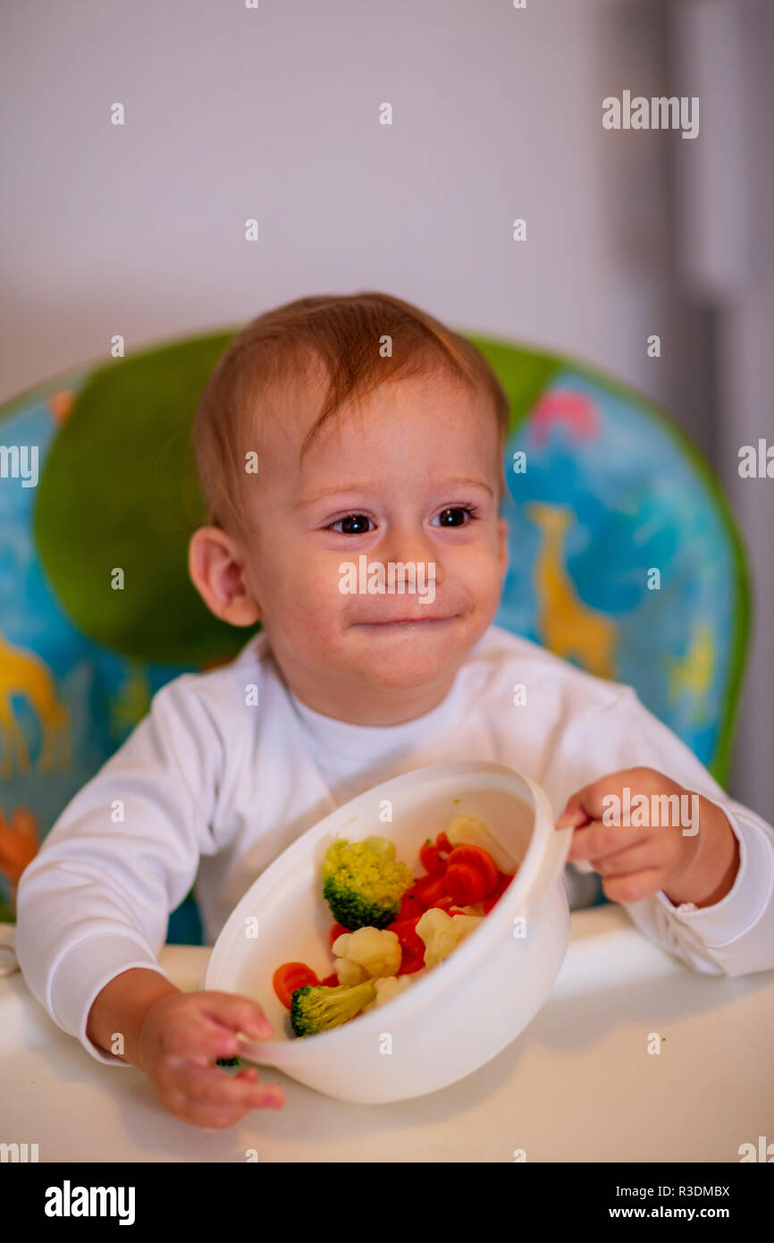 Children eat vegetables. Happy baby boy eating healthy vegetables Stock