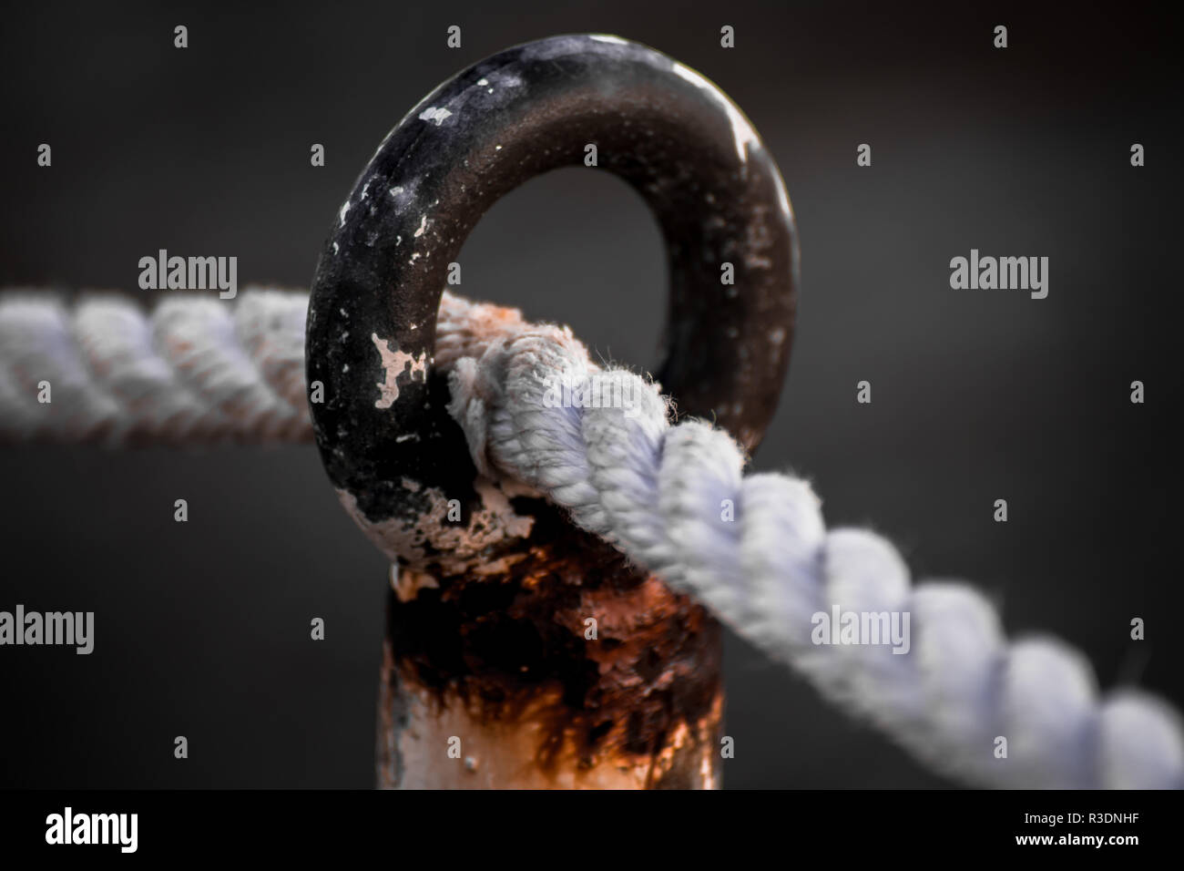 A white rope going through a rusty metal circle close to the sea Stock Photo