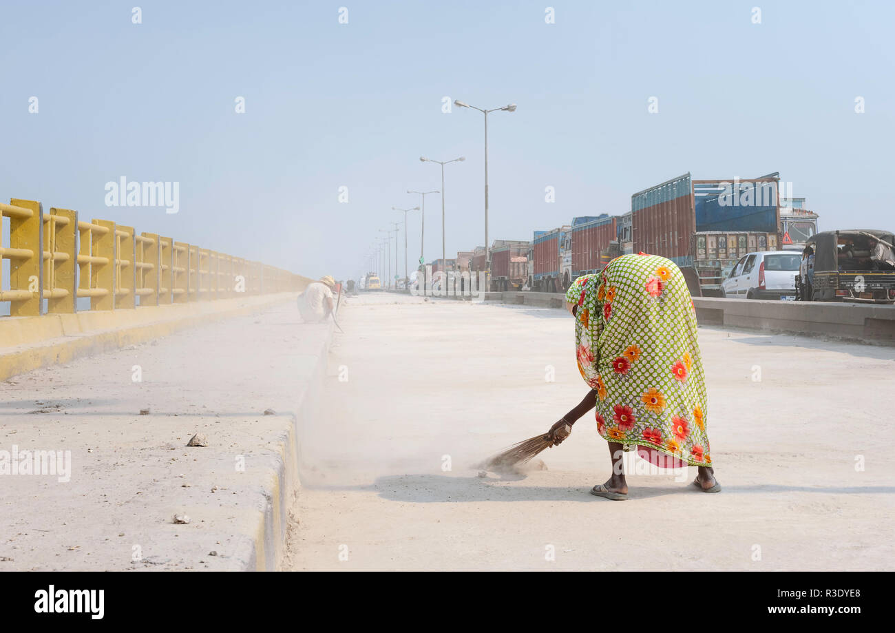 Woman sweeps one lane of the Mahatma Gandhi bridge during refurbishment and a long traffic jam on the other lane, Patna, Bihar, India. Stock Photo