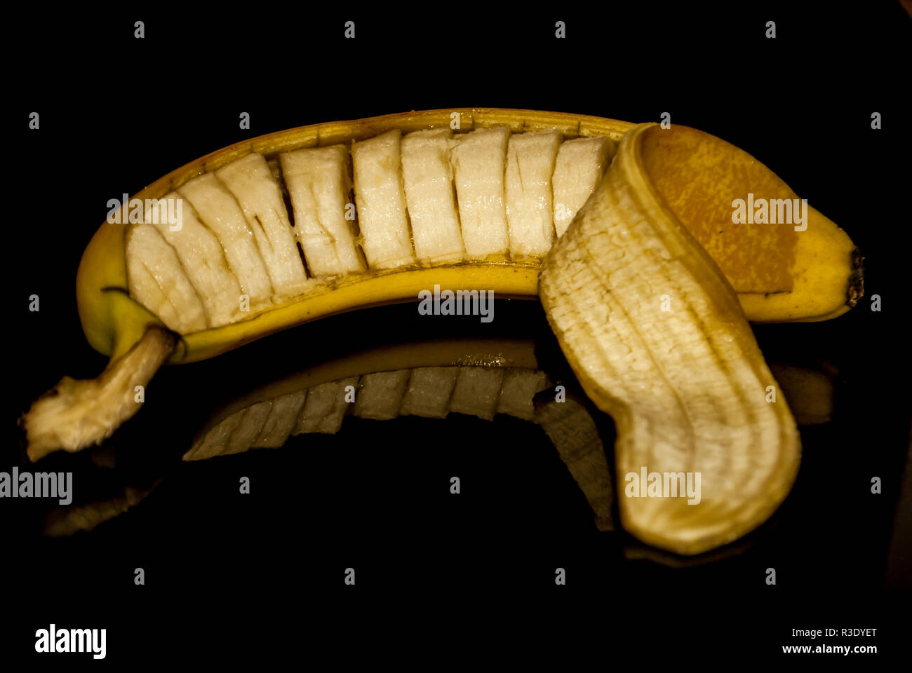 A cut banana still in its peel with a reflection against a black background Stock Photo