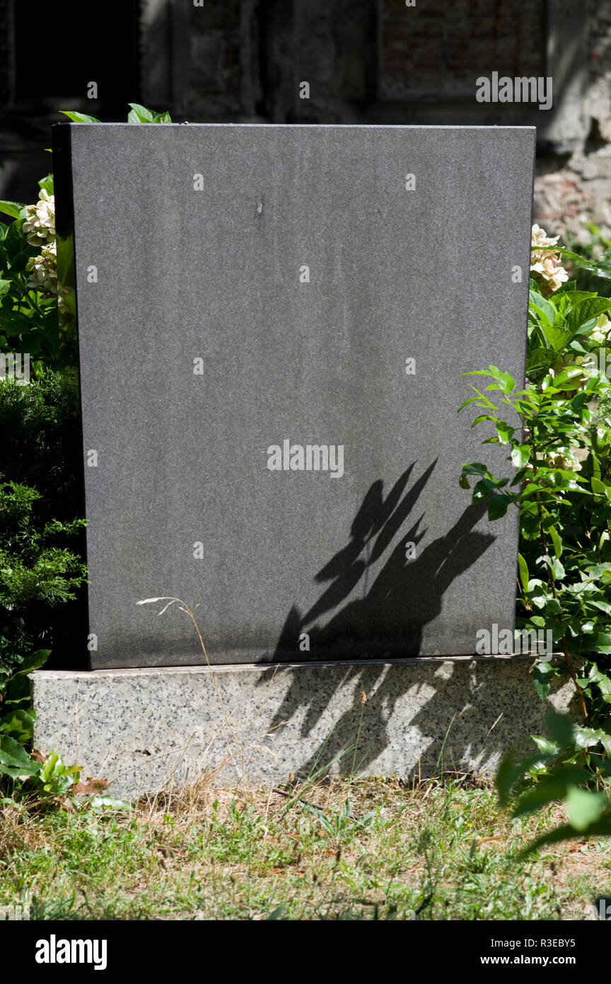 Austere headstone in a cemetery in Berlin, Germany with bright sunlight and shadows from a plant on the stone and no name engraved Stock Photo