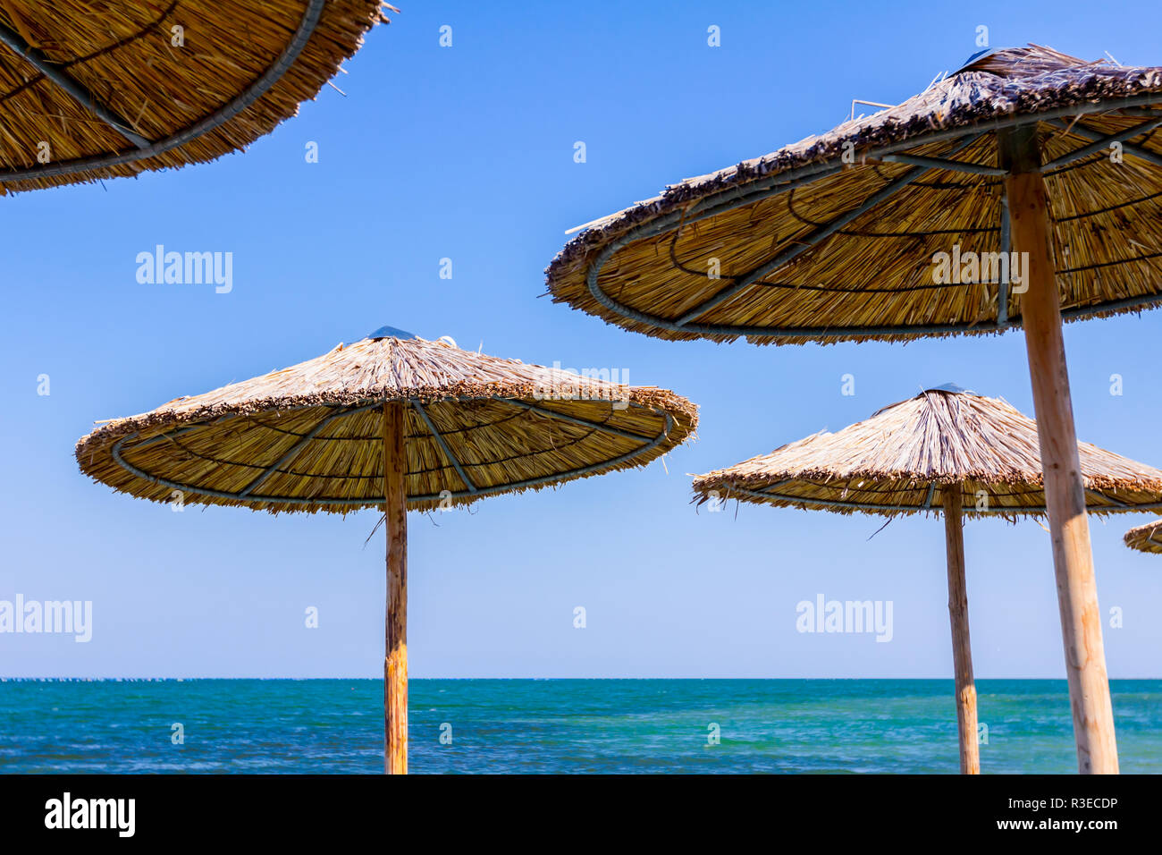 View on blue sea below thatched beach umbrella over blue sky. Sunshade made  with wood and reed on seascape Stock Photo - Alamy