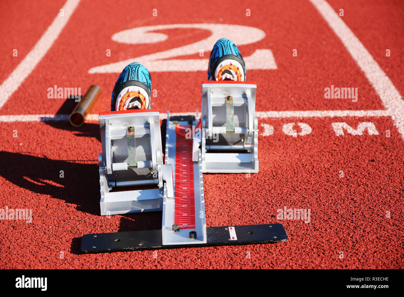 A set of starting blocks set up in lane 2 with a pair of spikes in them and a baton next to them ready for a race. Stock Photo