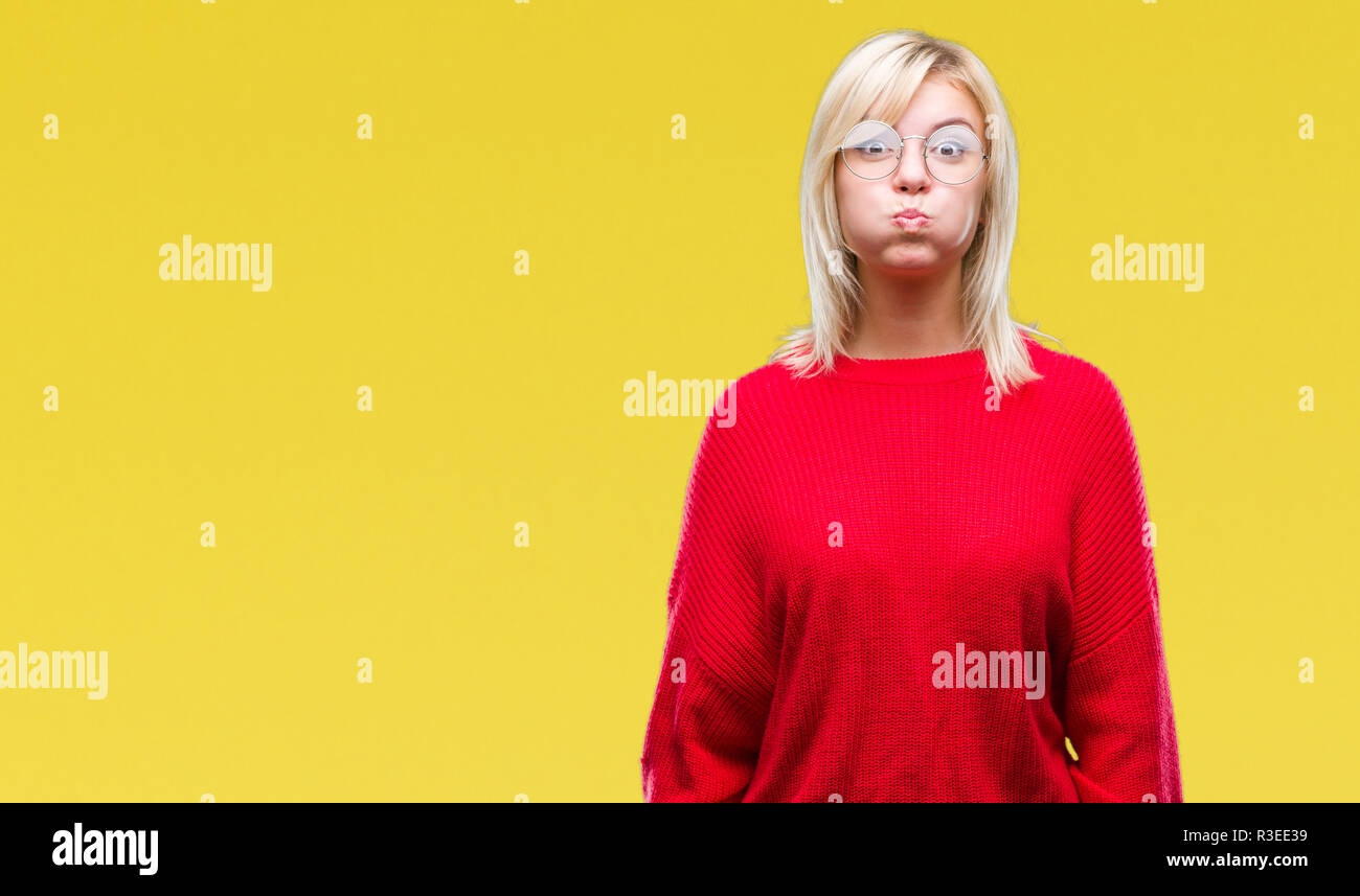 Young beautiful blonde woman wearing sweater and glasses over isolated background puffing cheeks with funny face. Mouth inflated with air, crazy expre Stock Photo